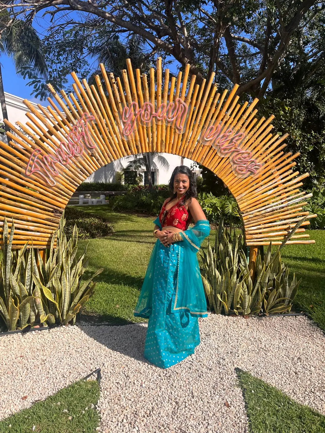 Santhra in her turquoise and red dance outfit beneath a sunburst installation